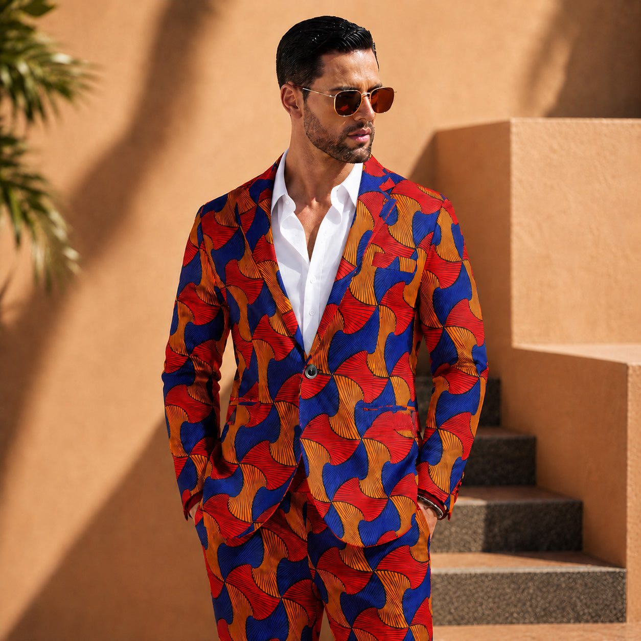 Model wearing a 2-piece vibrant African print men's suit with a blue, orange, and red geometric pattern, paired with a white dress shirt.