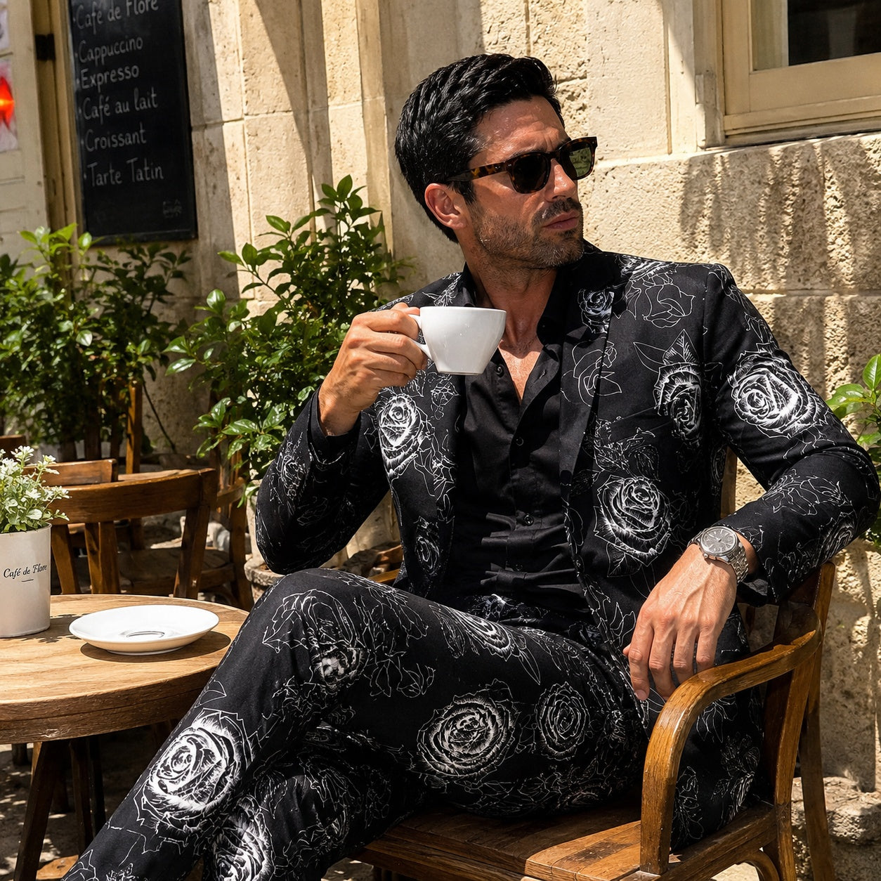 High-end men's floral suit in black and white, styled with sunglasses and a coffee at an outdoor cafe.