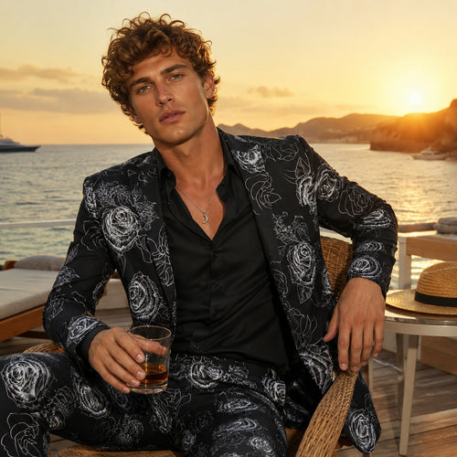 Man wearing a luxury white rose printed suit jacket with a black shirt, relaxing at a seaside resort.