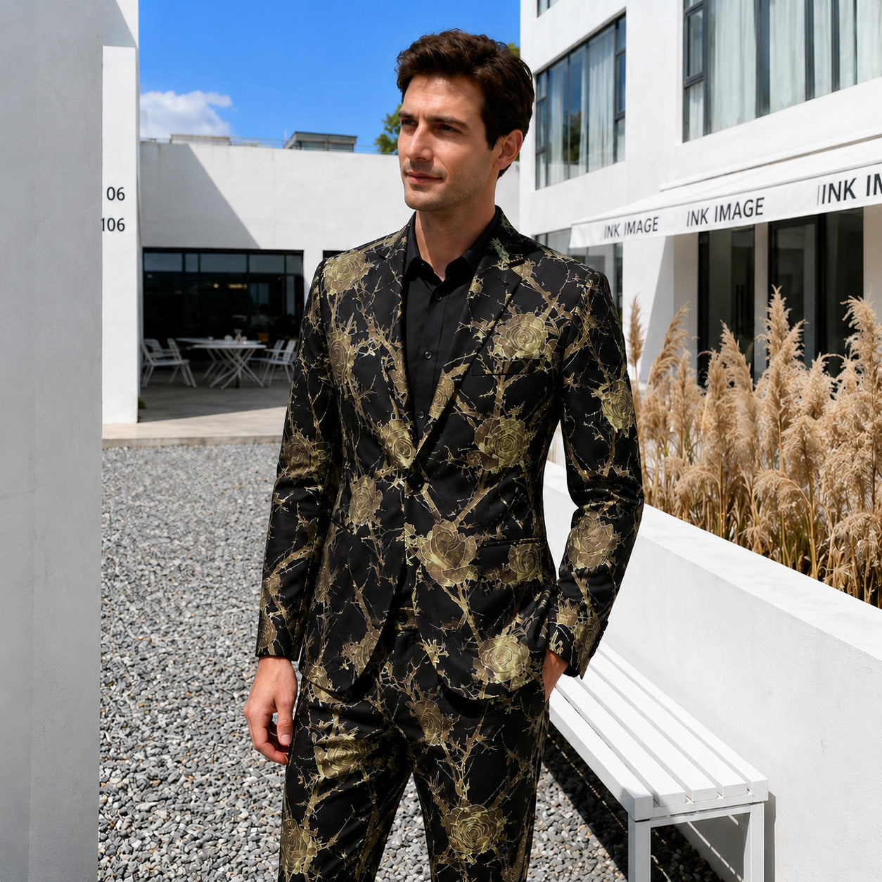 Model in a slim fit black suit with gold rose pattern standing outside a modern white building.