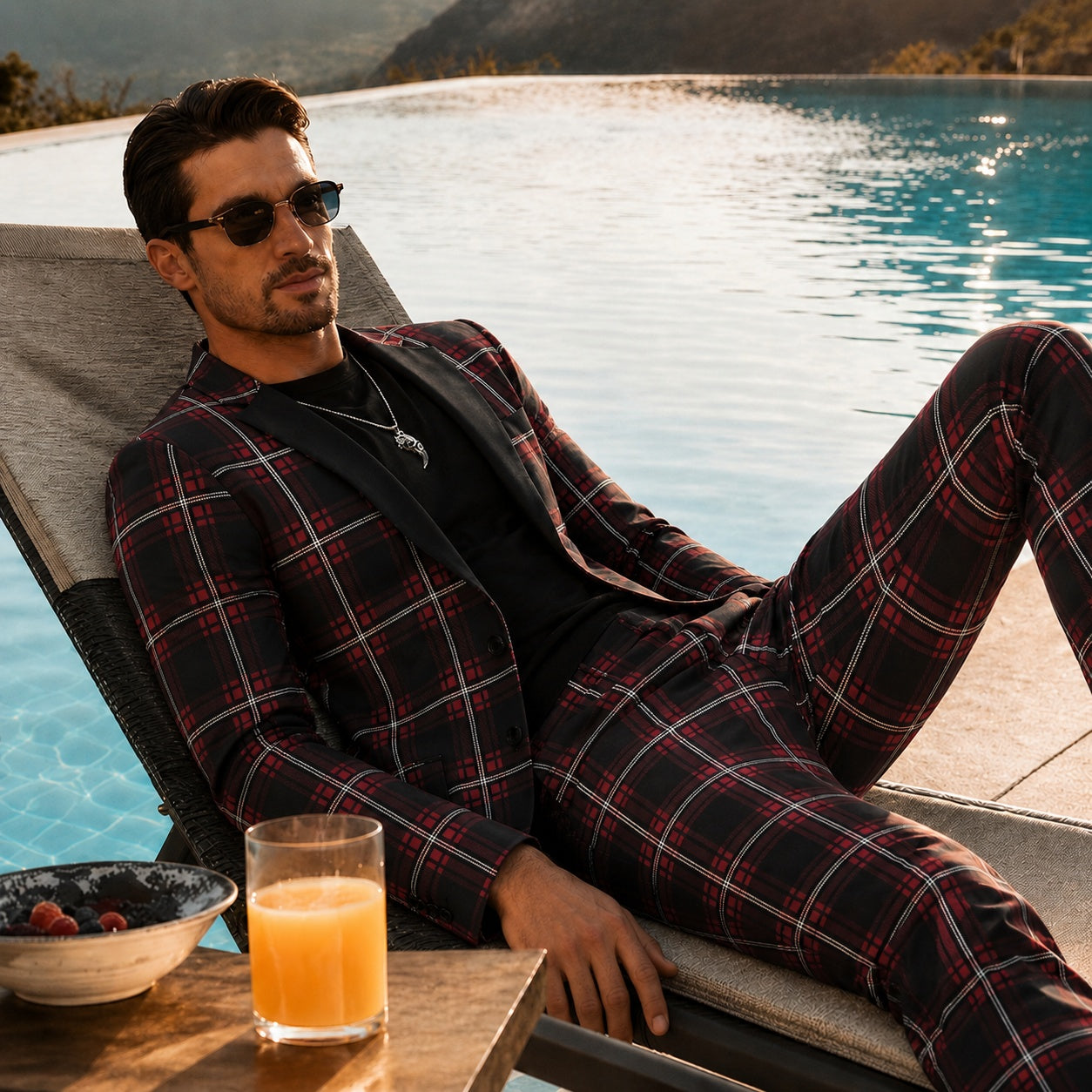 A man lounging by a luxury swimming pool wearing a sophisticated red and black tartan plaid suit for an effortless smart-casual look.
