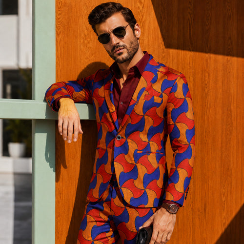 Side view of a stylish man leaning against a wooden wall, wearing an African Ankara print suit blazer with a burgundy button-down shirt and sunglasses.