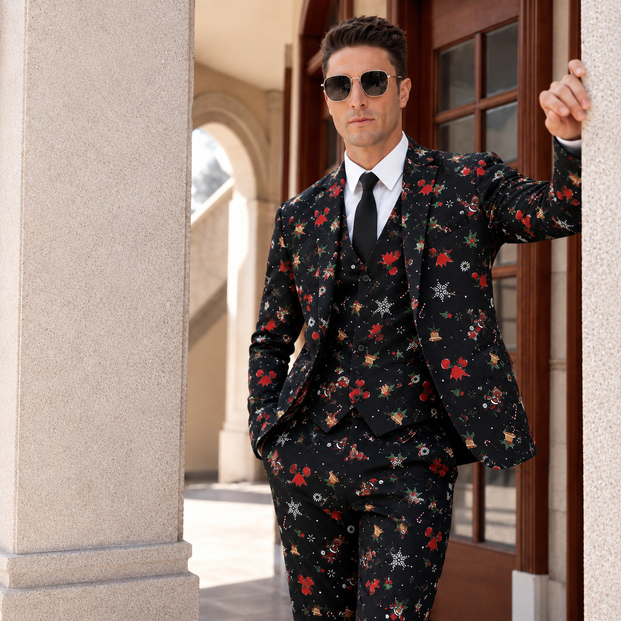 Man wearing sunglasses and a black 3-piece suit printed with Christmas bells and snowflakes, leaning against a building.