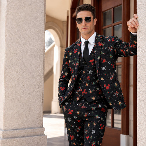 Man wearing sunglasses and a black 3-piece suit printed with Christmas bells and snowflakes, leaning against a building.