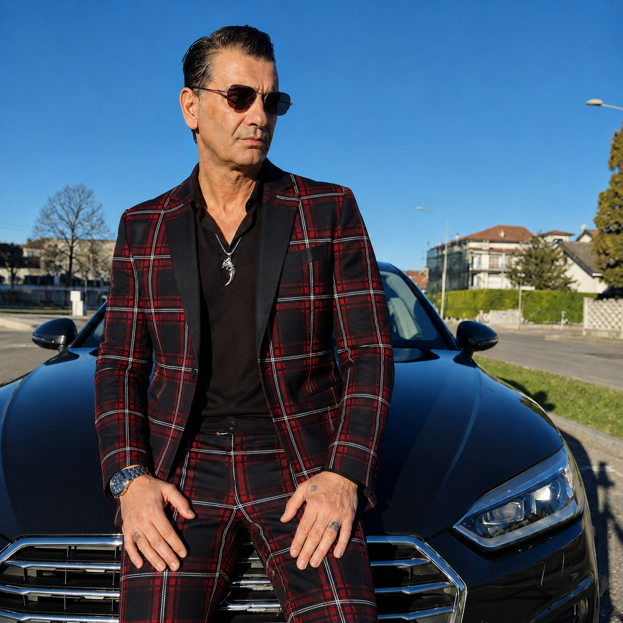 A sharp look featuring a men's red plaid blazer with black lapels paired with matching plaid trousers, leaning against a luxury black car.