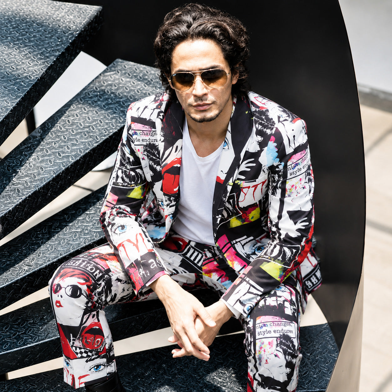 Side view of a man leaning on a balcony railing wearing a vibrant printed suit blazer with a black button-down shirt.