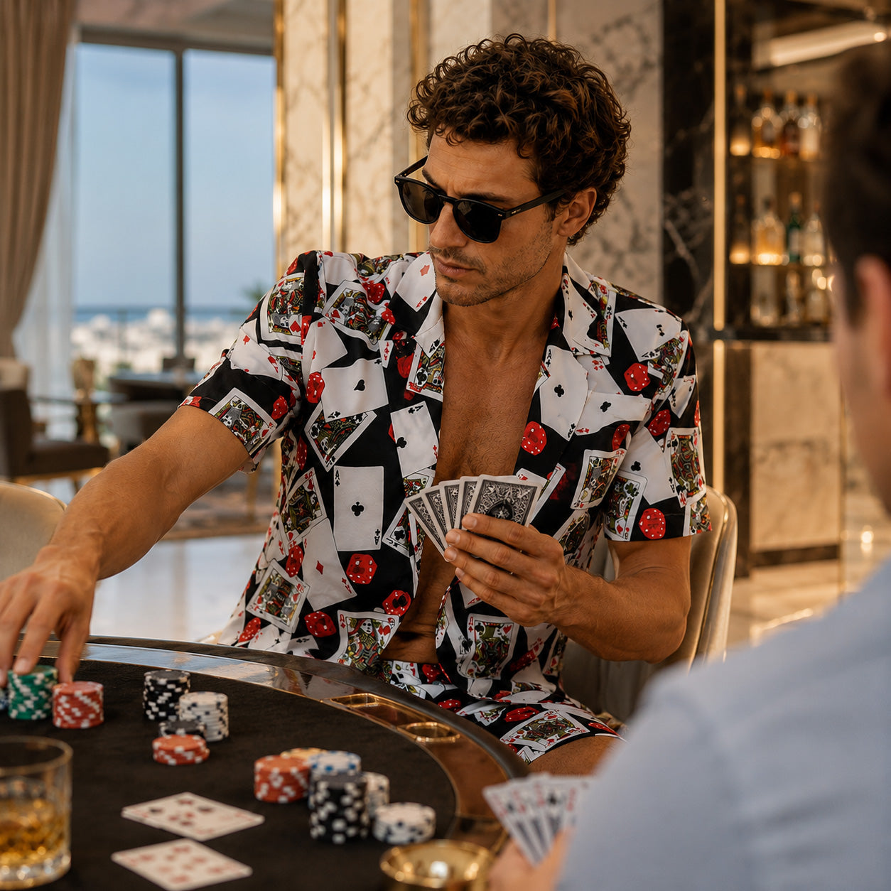 A close-up lifestyle shot of a man wearing an open poker print resort shirt while playing card games in a casino room.