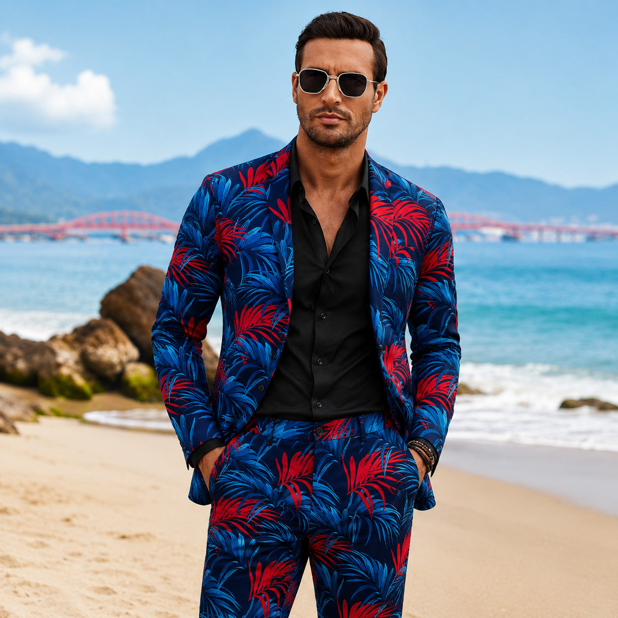 Fully styled men's slim fit suit in navy blue with red and blue tropical leaf prints, paired with a black unbuttoned dress shirt on a sunny beach background.