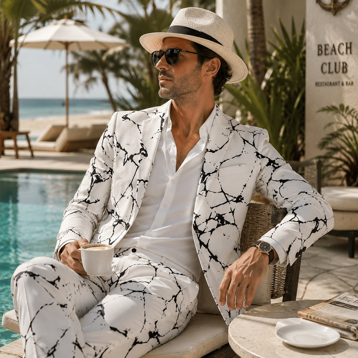 Handsome man wearing a modern white men's suit with black marble print pattern, relaxation by the pool at a beach club.