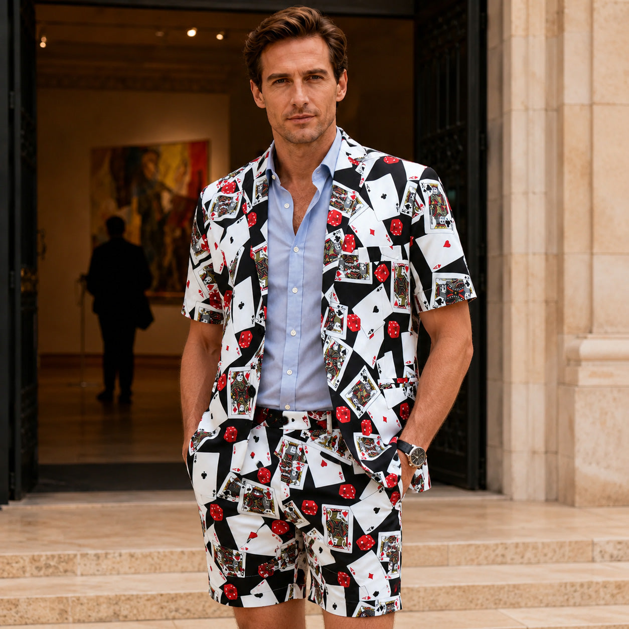 Man wearing a casino poker card print short-sleeve blazer and matching shorts set, paired with a light blue button-down shirt.