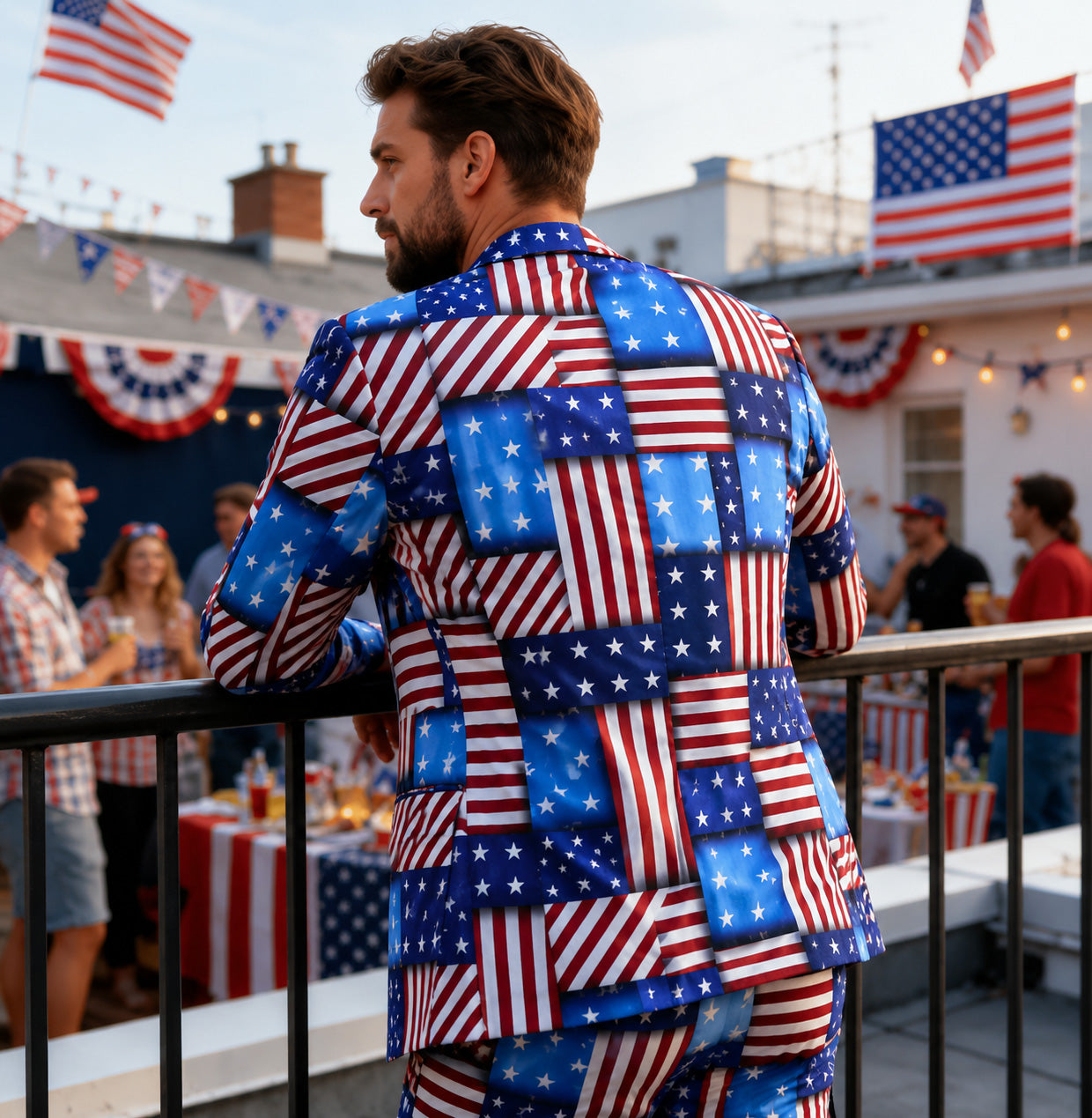 Back view of Wisholic American flag patchwork printed blazer and trousers ensemble on a man leaning on a rooftop railing during a 4th of July barbecue party.