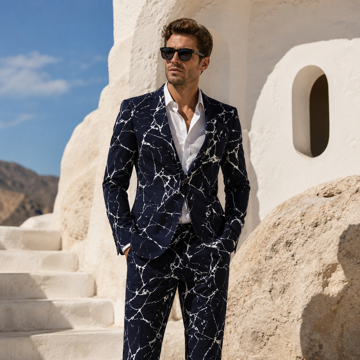 Premium artist design mens suit in deep navy with white marble texture, styled with sunglasses in front of a minimalist white Mediterranean architecture background.