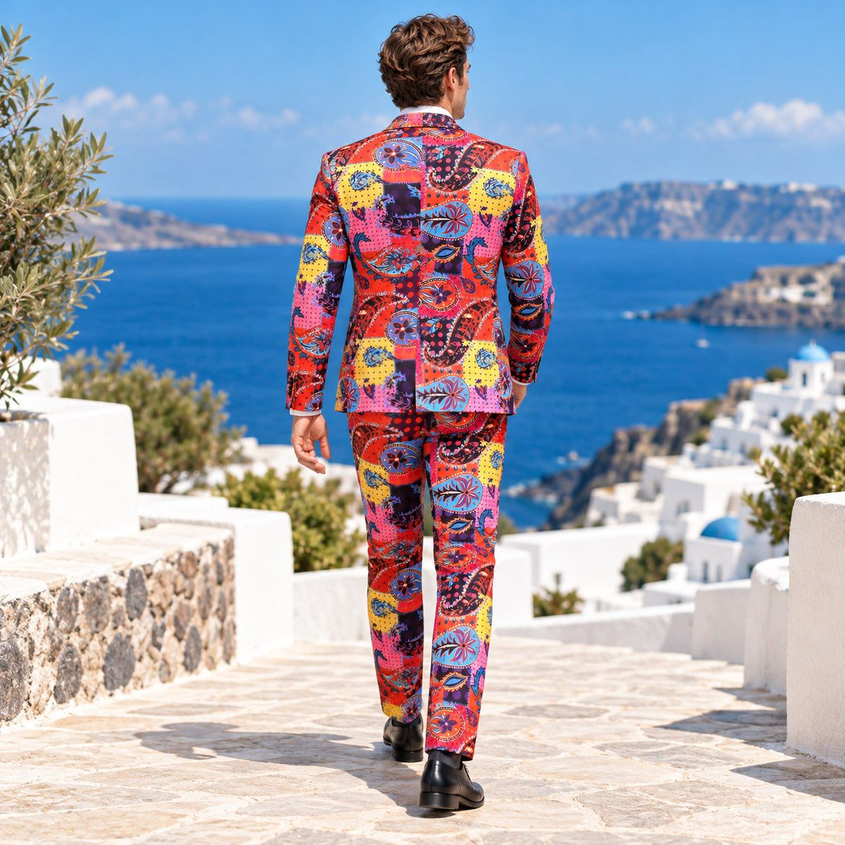Back view of WISHOLIC multicolor paisley men's suit showing the colorful patterned blazer and matching trousers against a Mediterranean coastal backdrop.