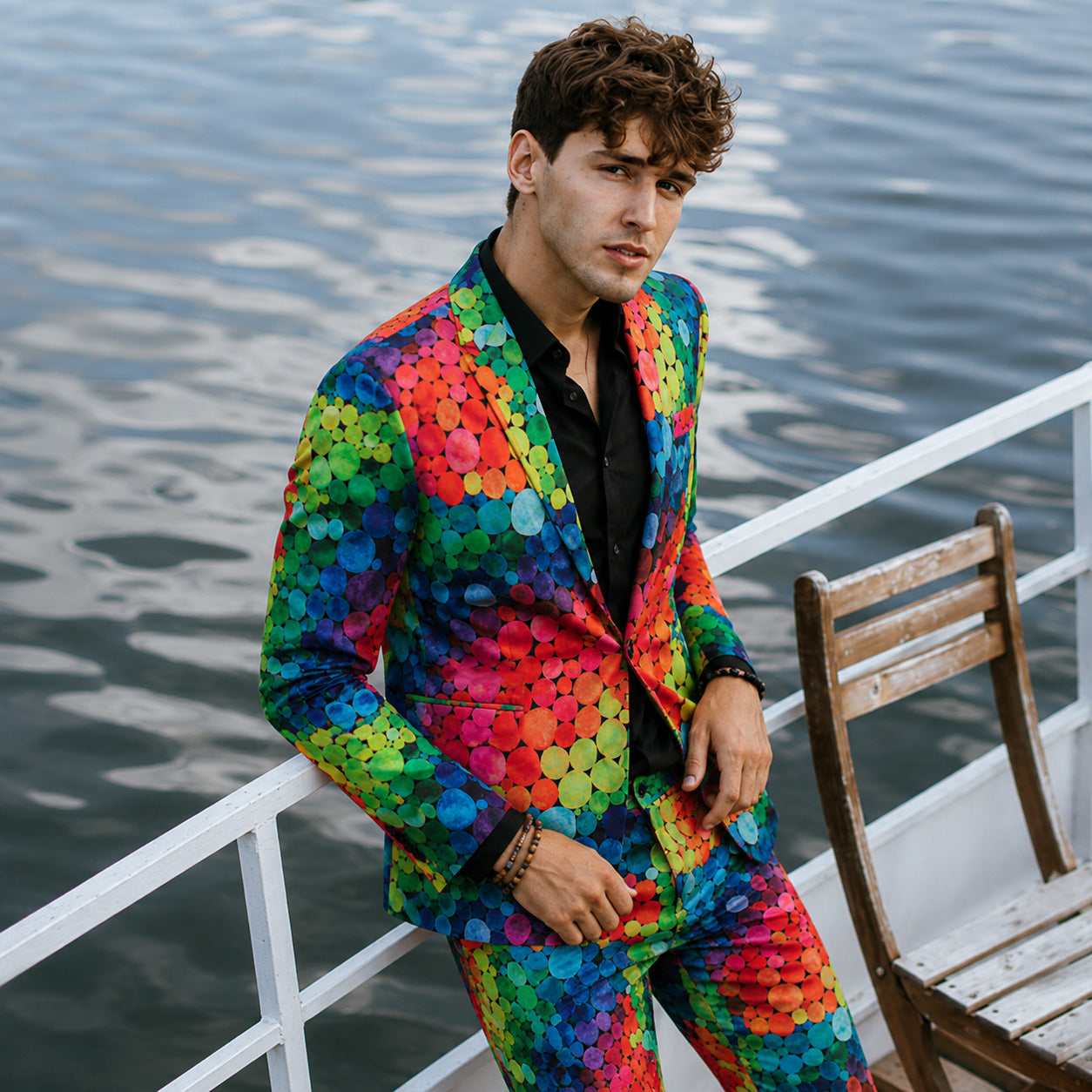 A model wearing the WISHOLIC vibrant rainbow polka dot suit leaning against a white railing on a boat or yacht.